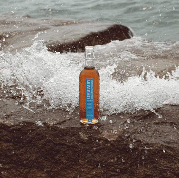 Bottle of Limavady whiskey on a beach with waves crashing around it.